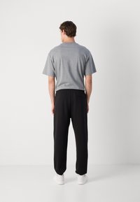 Grå bomulds t-shirt med korte ærmer og afslappet pasform, parret med sorte bukser med elastisk talje og hvide sneakers. Rent, minimalistisk design.