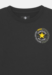 Sudadera negra de cuello redondo con una estrella amarilla y el logo "Converse All Star Established 1908" en la parte superior del pecho.