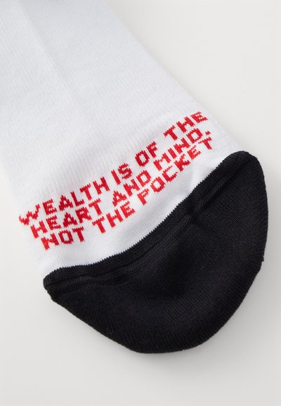 Chaussettes blanches avec un texte rouge qui dit "LA RICHESSE EST DANS LE COEUR ET L'ESPRIT, PAS DANS LA POCHE" avec un bout et un talon noirs.