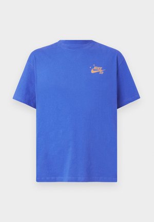 Camiseta de algodón azul con cuello redondo y mangas cortas. Presenta un pequeño logo naranja de Nike SB en el pecho. Textura suave.