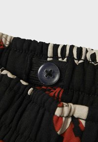 Geklede tailleband met een zwarte elastische band, decoratief bloemenpatroon in rood en crème, en een cirkelvormige zwarte knoopaccent.