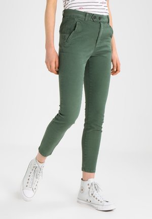 Gröna stretch chinos i slim fit med två framfickor och knappstängning, tillsammans med vita högskurna sneakers.