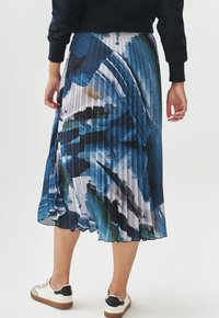 Plisseret midi-nederdel i blå, grøn og hvid abstrakt mønster. Letvægtsstof med en glat overflade. Båret med hvide sneakers.