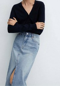 Cárdigan navy con un escote en V profundo y mangas largas, combinado con una falda de mezclilla ligera azul claro de cintura alta con una abertura. Textura suave.