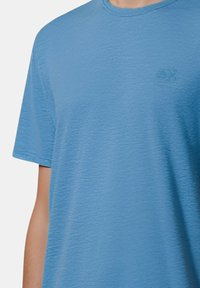T-shirt azzurro chiaro con scollo tondo realizzato in un tessuto morbido e testurizzato. Maniche corte con un discreto logo ricamato sul petto.
