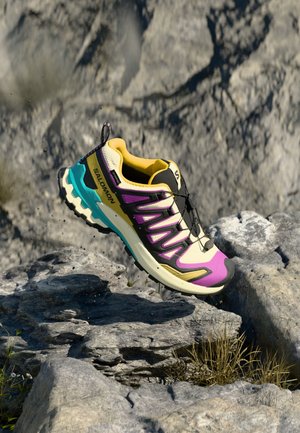 Multi-colored athletic shoe with a yellow and purple upper, black accents, and a turquoise sole, featuring a textured mesh design and lacing system.