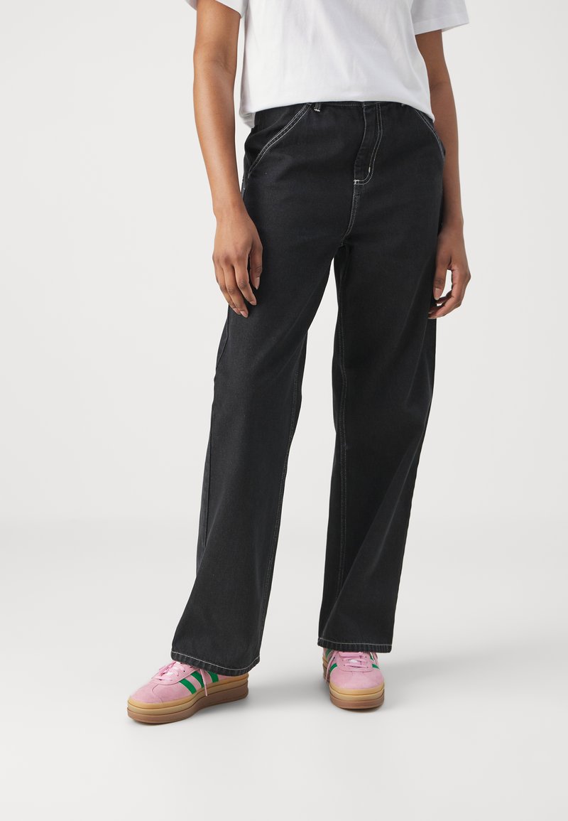 Sorte denim bukser med vide ben, sidelommer, kontrastsyninger og høj talje. Båret med pink sneakers med grønne striber.