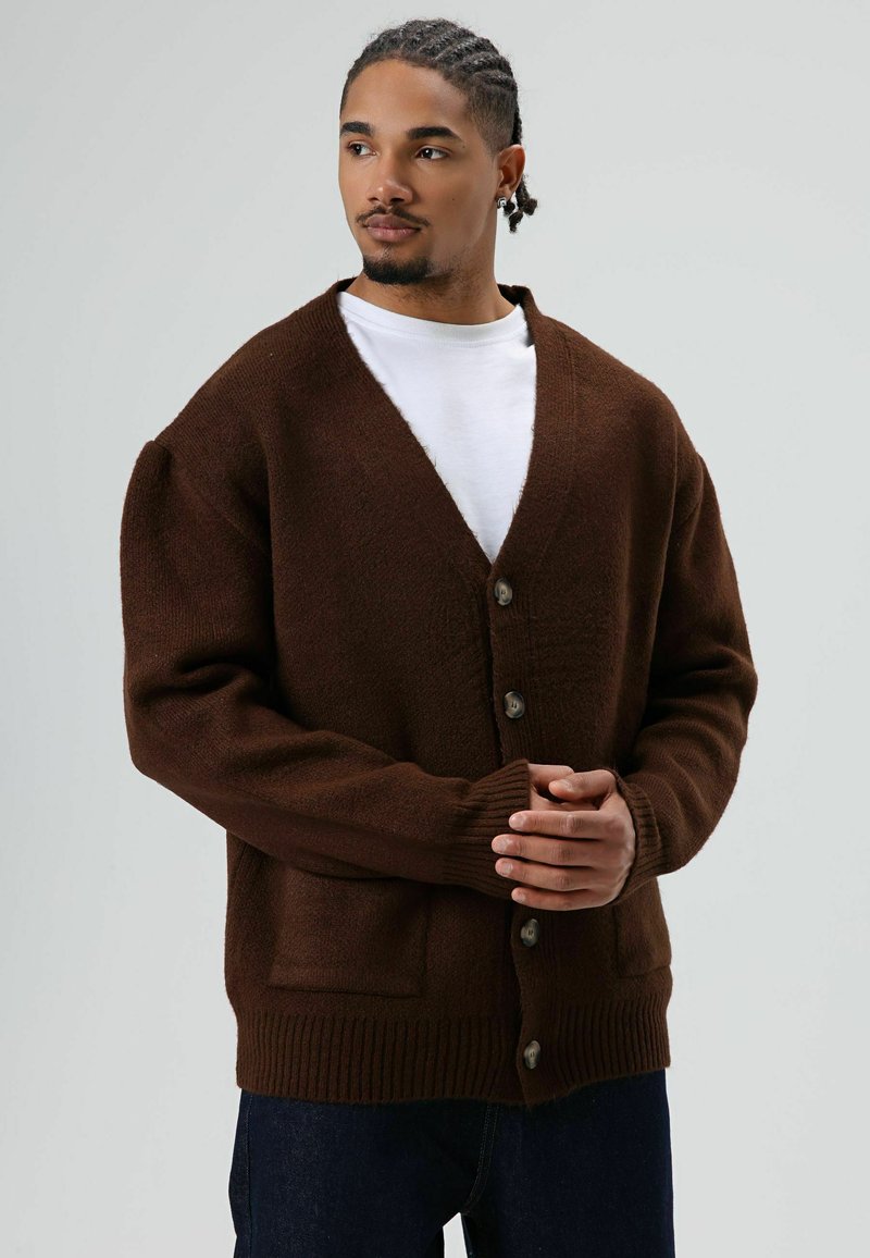 Cardigan brun en tricot avec col en V, manches longues, boutons devant et deux poches ; présente une finition texturée et des poignets côtelés.