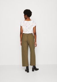Haut à manches courtes à imprimé floral en blanc et couleurs pastel, associé à un pantalon ample vert olive et des bottines noires à talon carré.