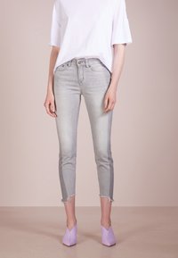 Jeans skinny grigio chiaro con orlo grezzo, abbinati a una t-shirt bianca ampia e décolleté lavanda con punta a spillo, che mostrano un abbinamento da outfit casual.