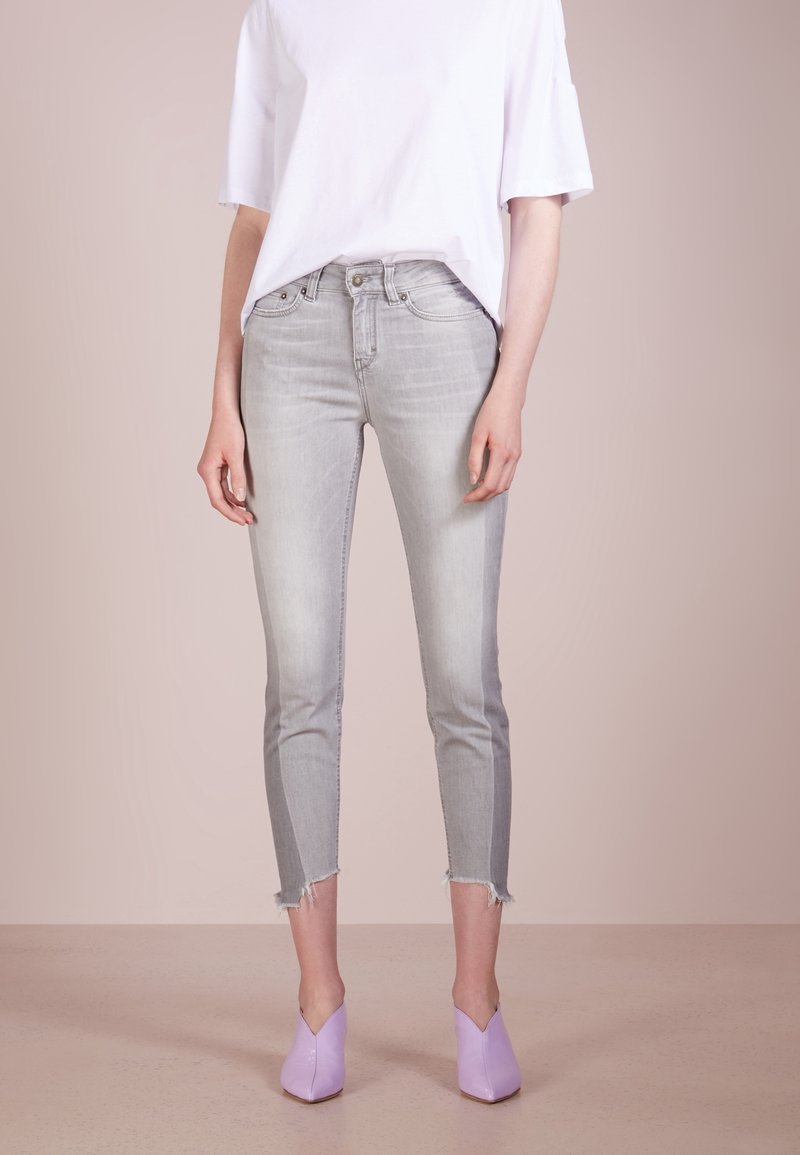 Jeans skinny grigio chiaro con orlo grezzo, abbinati a una t-shirt bianca ampia e décolleté lavanda con punta a spillo, che mostrano un abbinamento da outfit casual.