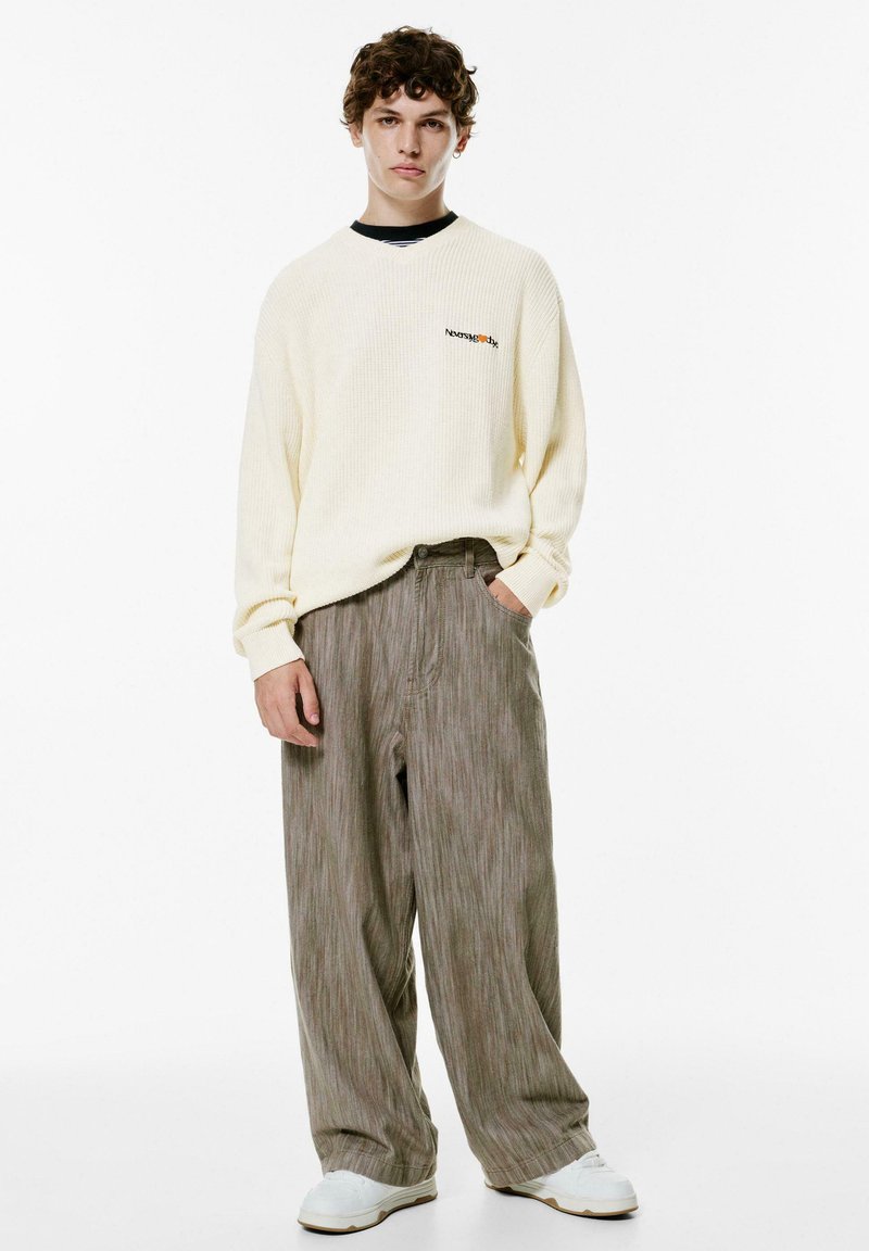 Kerma ribbad tröja med logga, i kombination med löst sittande olivgröna randiga byxor och vita sneakers, vilket skapar en avslappnad, ledig look.