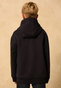 Schwarzer Kapuzenpullover mit entspannter Passform, ausgestattet mit einer gefütterten Kapuze und gerippten Bündchen. Texturiertes Gewebe, keine sichtbaren Marken oder Muster.