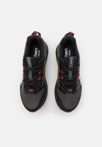Baskets de course noires avec une tige texturée, accents jaunes et violets, dotées d'un col rembourré et d'une semelle à motifs.