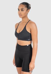 Mustat urheiluliivit, joissa on kerrostettu etuosa, ohuet olkaimet ja brändätty vyö. Yhdistetty korkeavyötäröisiin mustiin shortsit, molemmat sileää kangasta.