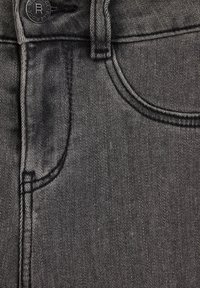 Mörkgrå denimtyg med en närbild av ett fickområde, med synlig sömnad och en metalldetalj med knapp.