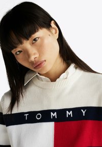 Strikket sweater med hvid base, marineblå og røde vandrette striber samt "TOMMY" broderet i hvidt tværs over brystet. Tekstureret stof.