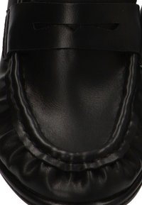 Zapato negro de cuero sin cordones con puntera redondeada y textura arrugada alrededor del borde. Presenta una tira horizontal a lo largo del empeine.