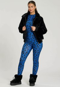 Chaqueta bomber de pelo sintético negro sobre un body azul con estampado de leopardo negro. Botines negros esponjosos con suelas gruesas completan el conjunto.