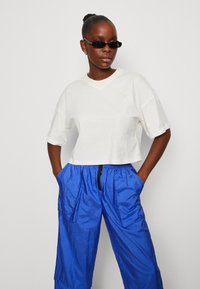 T-shirt bianco di cotone cropped con un logo sottile, abbinato a pantaloni in nylon blu brillante dalla vestibilità ampia, dotati di tasche e vita elasticizzata.