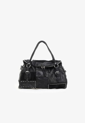 Bolso de mano de patchwork de cuero negro con tachuelas plateadas, dos asas, cremalleras frontales y correas decorativas con hebilla sobre un fondo blanco.