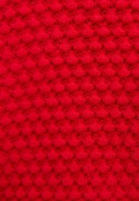 Gros plan d'un tissu en tricot rouge avec des points texturés et bouclés, ainsi que des fibres de laine douces.