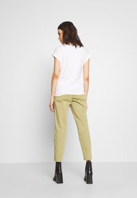 Camiseta blanca de manga corta combinada con pantalones ajustados verde claro y botas de tobillo negras con plataforma, vista desde la parte de atrás.