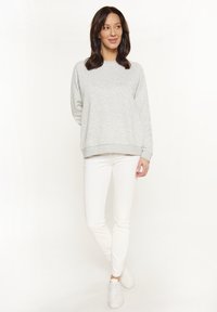 Felpa grigia con scollatura rotonda e maniche lunghe, abbinata a pantaloni bianchi aderenti e sneakers bianche. Outift semplice e informale.