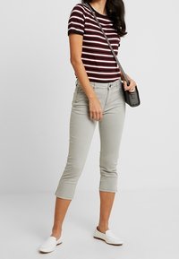 T-shirt a righe bordeaux e bianche, pantaloni grigi a vita alta, e scarpe bianche slip-on; presenta una vestibilità slim e una borsa a tracolla nera minimal.