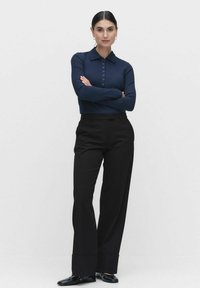 Tummansininen ribattu pitkähihainen polo paita, jossa on kaulus ja nappilista, yhdistettynä korkea vyötäröisiä mustia housuja ja mustia kenkiä.