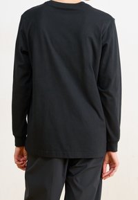 Svart långärmad t-shirt i bomull med rundad halsringning och avslappnad passform, med stickade sömmar och en mjuk textur.