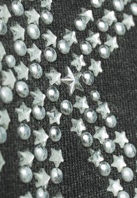 Tela negra con adornos plateados en forma de estrella y redondos de varios tamaños que crean un patrón decorativo en toda la superficie.