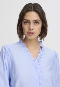 Lichtblauwe blouse met knopen, gemaakt van zachte stof, met een geraffineerde halslijn en pofmouwen, met een gladde textuur en een relaxte pasvorm.