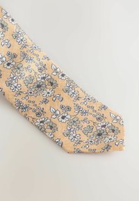 Cravate florale jaune présentant un motif de fleurs bleues et blanches avec des feuilles vertes, fabriquée en tissu texturé, conception à bout effilé.