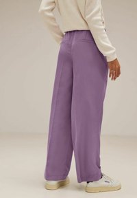 Lila vida byxor med en slät textur, med hög midja och bakfickor, kombinerat med vita sneakers.