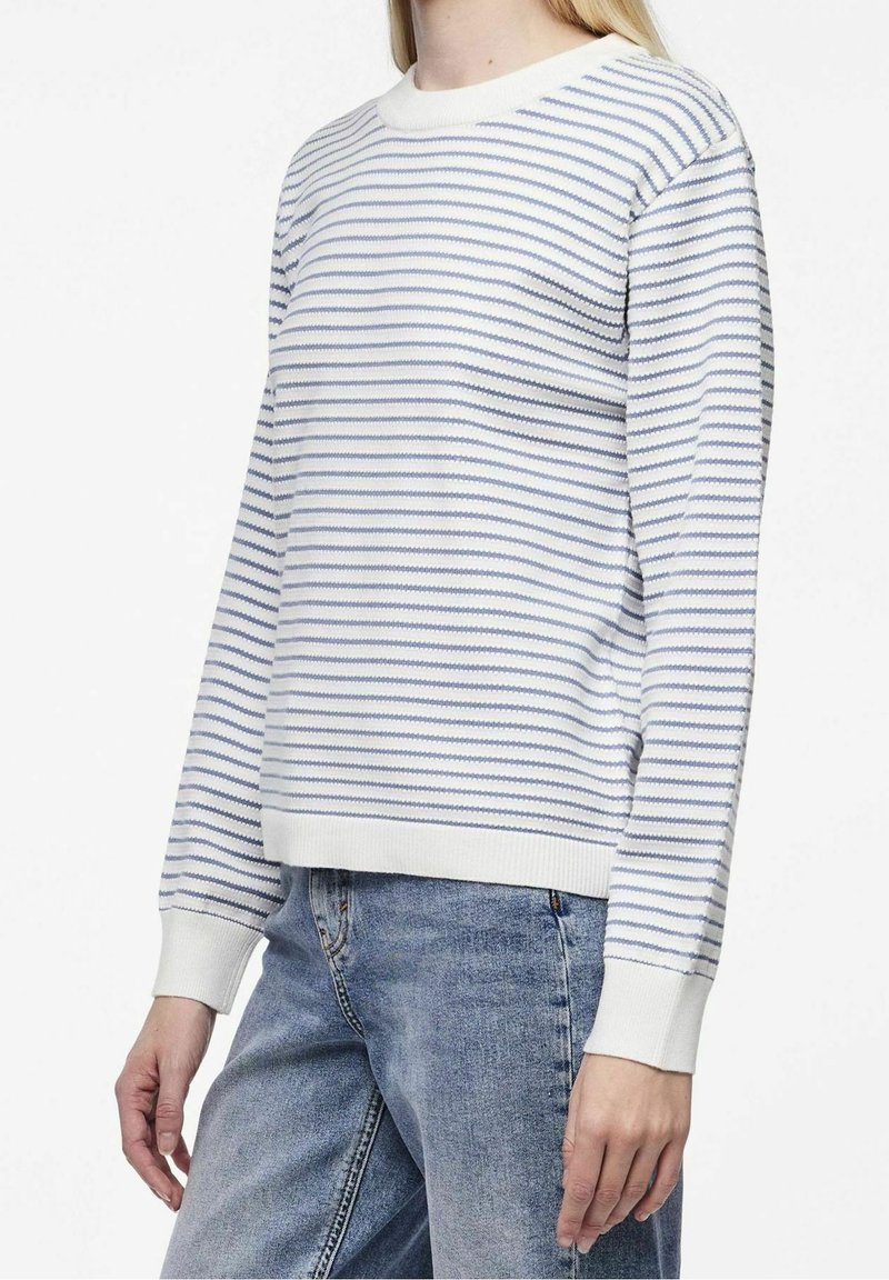 Biały sweter z poziomymi niebieskimi paskami, z prążkowanym dekoltem i mankietami, o luźnym kroju i miękkiej fakturze. W połączeniu z niebieskimi dżinsami.