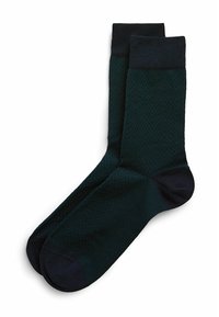 Calcetines de color verde oscuro con un patrón de espiga, que presentan un puño y una puntera en azul marino sólido. Están hechos de un material texturizado para mayor comodidad.