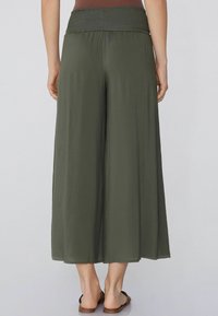 Široké olivové kalhoty s nařaseným pasem, vyrobené z lehké látky, sahající po polovinu lýtek, stylizované s plochými sandály.