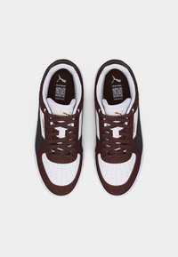 Ζεύγος καφέ και λευκών αθλητικών παπουτσιών Puma με μαύρο λογότυπο στο πλάι, καφέ κορδόνια και κωδικούς QR μέσα στις φτέρνες, τοποθετημένα σε λευκό φόντο.