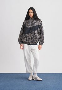 Μαύρο και μπεζ μπουφάν με λεοπάρ σχέδιο, φερμουάρ μπροστά, μανίκια balloon και μαύρη πινελιά· συνδυασμένο με ανοιχτό γκρι παντελόνι με φαρδιές μπατζάκια και αθλητικά παπούτσια.