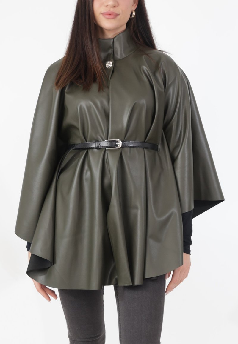 Olijfgroene cape van imitatieleer met een hoge kraag, vastgemaakt met een zwarte riem. Heeft een glanzende zilveren knop bij de kraag.