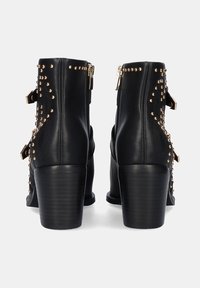 Botines de cuero negro con tachuelas doradas, cremalleras laterales y dos correas decorativas. Tacón grueso con un acabado texturizado.