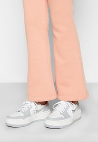 Weiße und graue Sneaker mit strukturiertem Obermaterial, ausgestattet mit Perforationen und einer dicken Sohle, kombiniert mit hellrosa, ausgestellten Sweatpants.