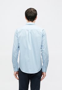 Chemise à manches longues bleu clair avec un motif subtil, poignets à boutons, et une coupe droite. Tissu lisse et col classique.
