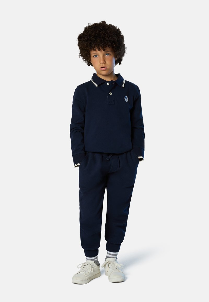 Polo blu navy a maniche lunghe con accenti bianchi sul colletto, abbinato a joggers blu navy coordinati. Tessuto in cotone morbido e sneakers bianche completano l'outfit.