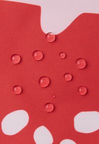 Rode textuurstof met witte organische vormen en verschillende heldere waterdruppels die op het oppervlak liggen.