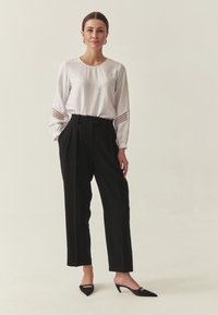 Haut blanc à manches longues avec des accents texturés aux poignets, associé à un pantalon noir taille haute et des mules noires à talons. Design simple et élégant.