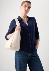 Marineblå knappeskjorte med lange ermer, kombinert med lyseblå jeans og en kremfarget skulderveske, som fremviser glatt stoff og rene linjer.