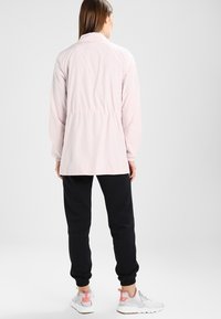 Růžová lehká bunda s elastickým pasem, dlouhými rukávy a límcem, doplněná černými tepláky a bílými teniskami s růžovými prvky.