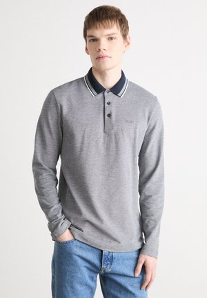 Polo gris à manches longues avec un col bleu marine, patte de boutonnage à deux boutons et un logo discret, associé à un jean bleu. Tissu lisse et texturé.